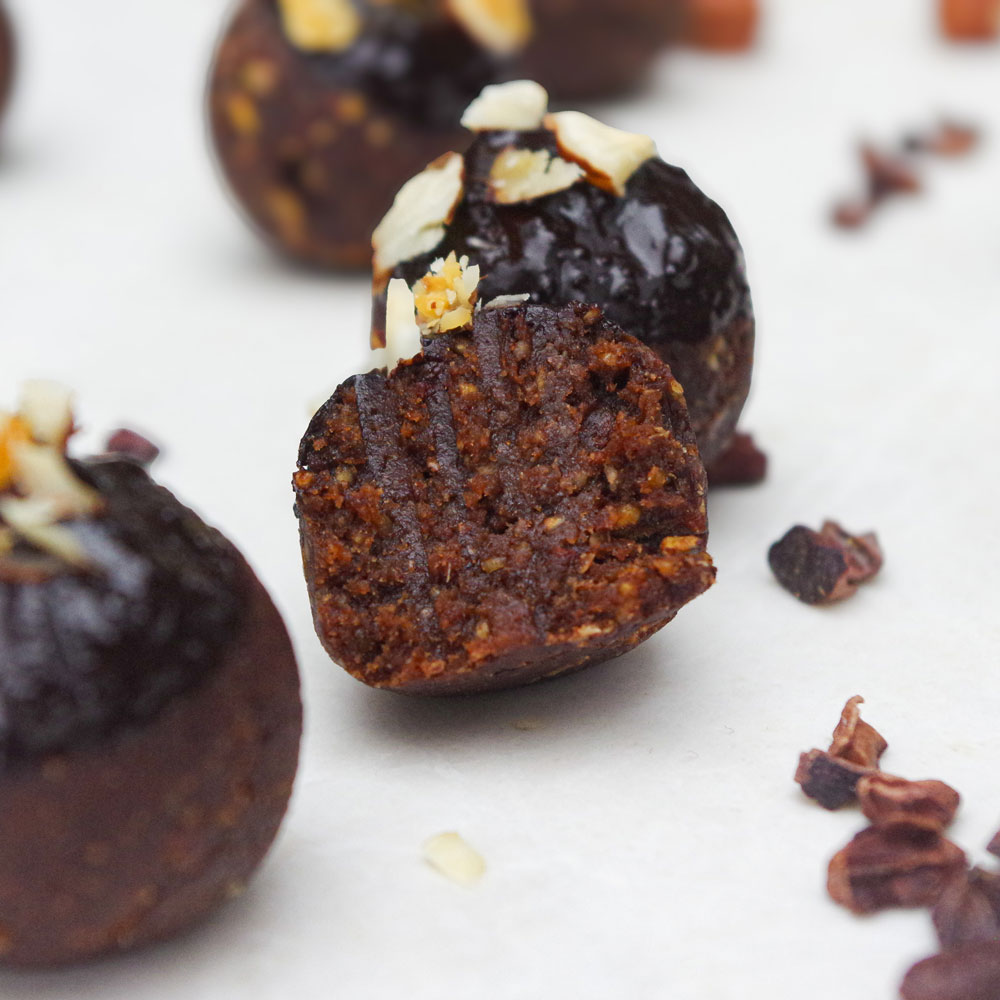 Nahaufnahme von angebissenem proteinreichen Energiebällchen mit Haselnüssen und Kakaonibs.